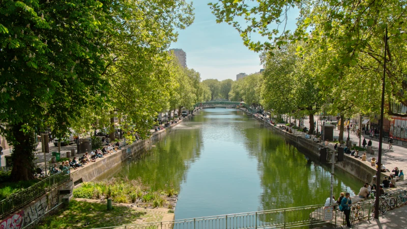 Strolling along the Canal Saint-Martin in Paris with people relaxing on the banks under lush green trees.