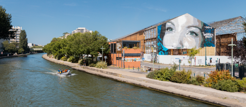 The Canal de l'Ourcq in Paris with a boat passing near a street art mural