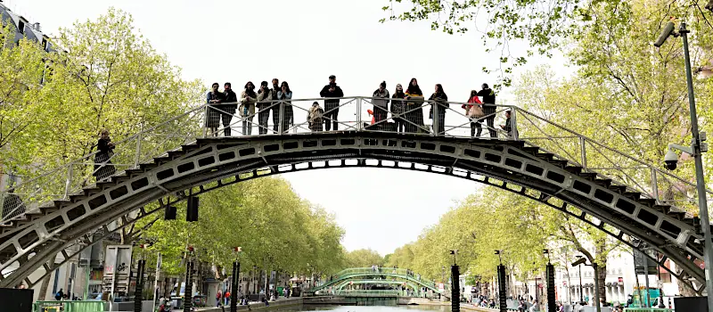 Tourists on a bridge over the Canal Saint-Martin in Paris, surrounded by greenery